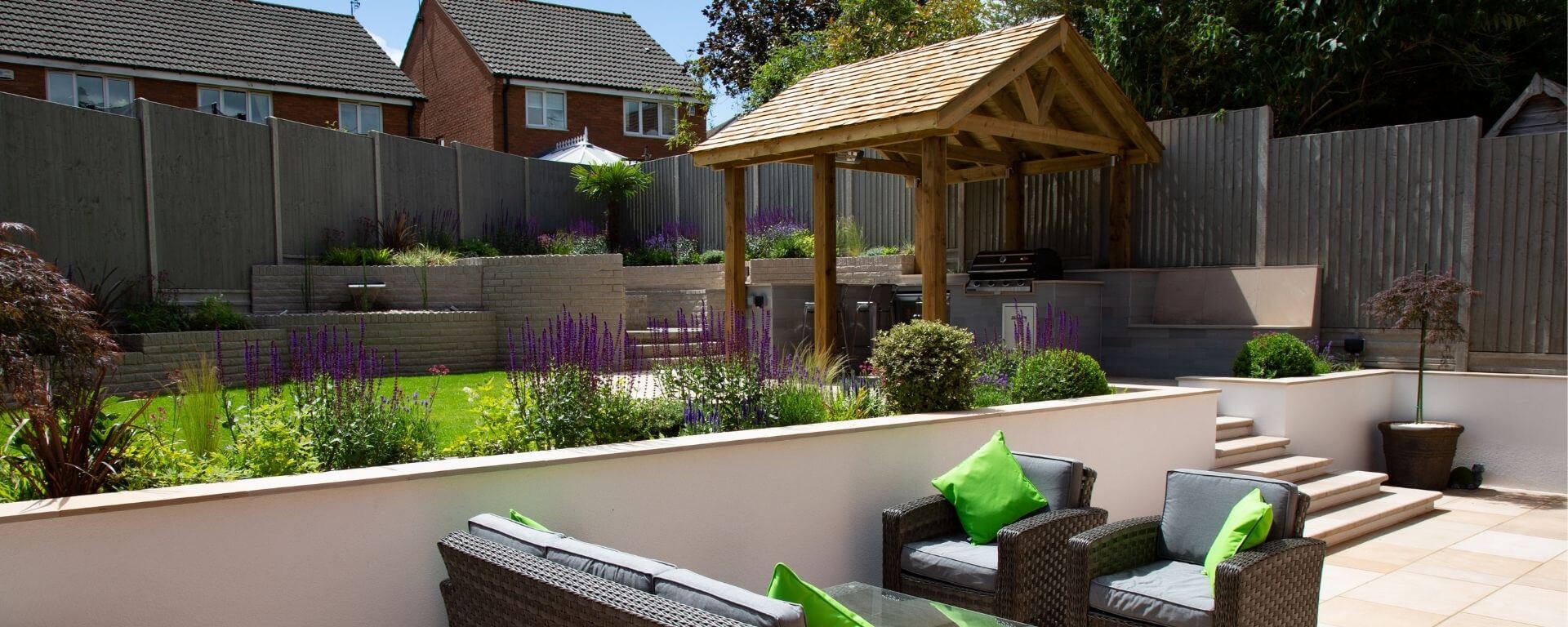 A two tier garden with white rendered walls, outdoor kitchen and fire pit area
